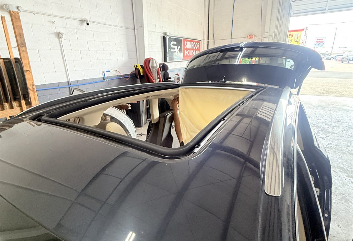 Custom sunroof glass tilted open on a dark vehicle with the interior covered for protection during installation at Sunroof King