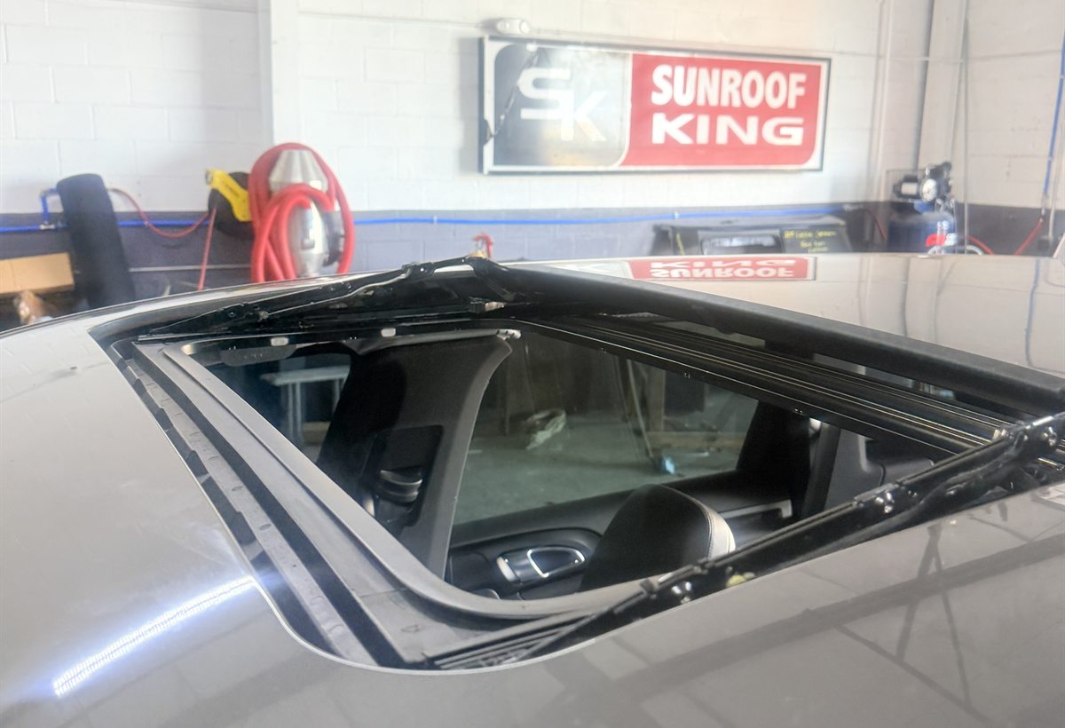 Freshly cut sunroof opening and seal channel in a dark vehicle roof beneath the Sunroof King sign in Houston