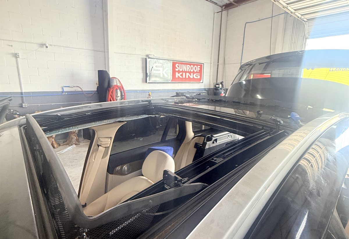 Sunroof opening cut into a vehicle roof with the frame fitted, seen from above inside the Sunroof King shop in Houston