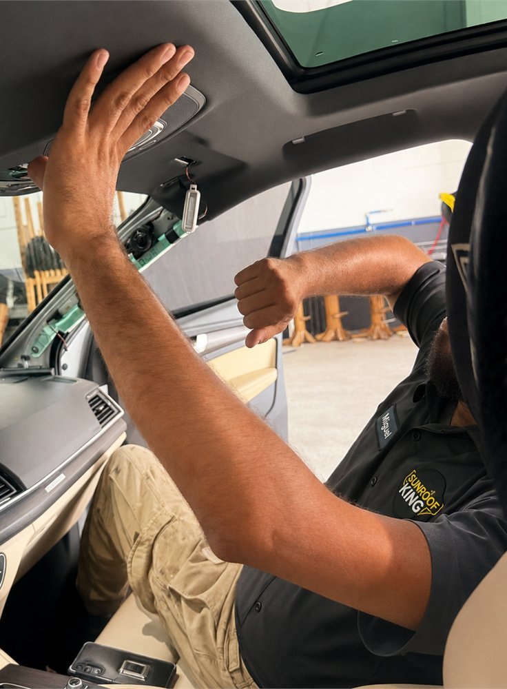 Sunroof King technician in the branded black uniform reaching up to the headliner and sunroof opening from inside a vehicle