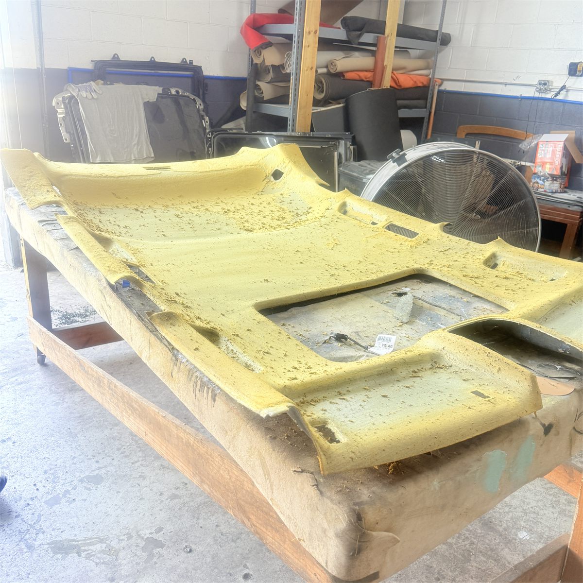 Headliner board on the workbench at Sunroof King with the old fabric stripped off and deteriorated foam residue exposed, cut for a sunroof opening