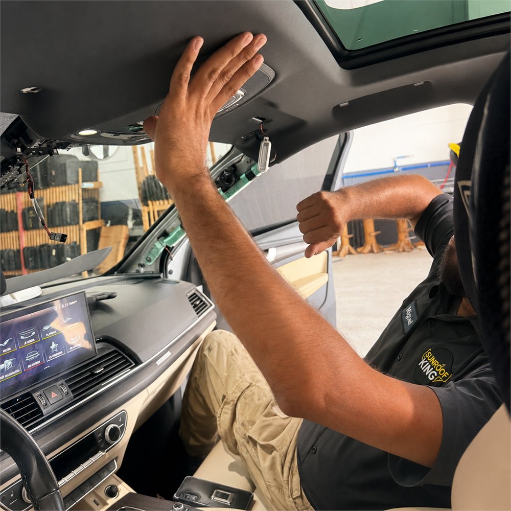 Sunroof King technician in branded black uniform working at the headliner inside a vehicle at the Houston shop