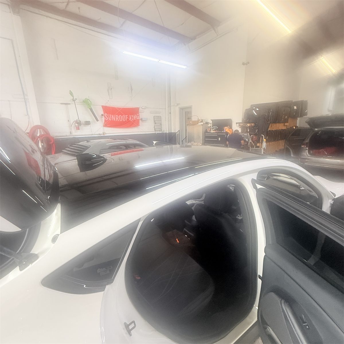 Large panoramic glass panel lifted off a vehicle roof inside the Sunroof King shop in Houston