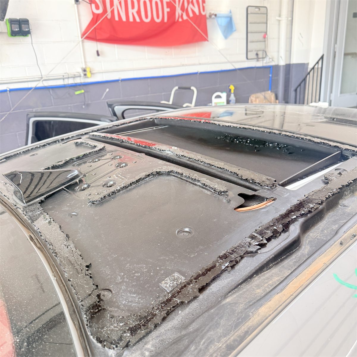 A sunroof glass panel lifted out of a vehicle roof at the Sunroof King shop in Houston, exposing the frame, the perished seal around the aperture and a second roof opening behind it