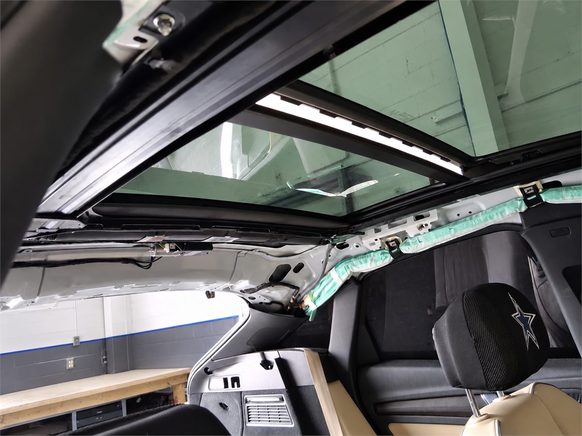 Panoramic roof glass seen from inside a vehicle at Sunroof King in Houston with the headliner removed, exposing the roof frame, side rails and wiring above the seats