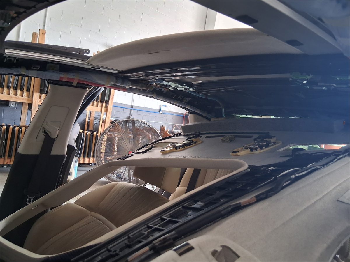 Interior of a vehicle at the Sunroof King shop in Houston with the headliner lowered, showing the roof structure, the sunroof frame and the shade panel above the seats