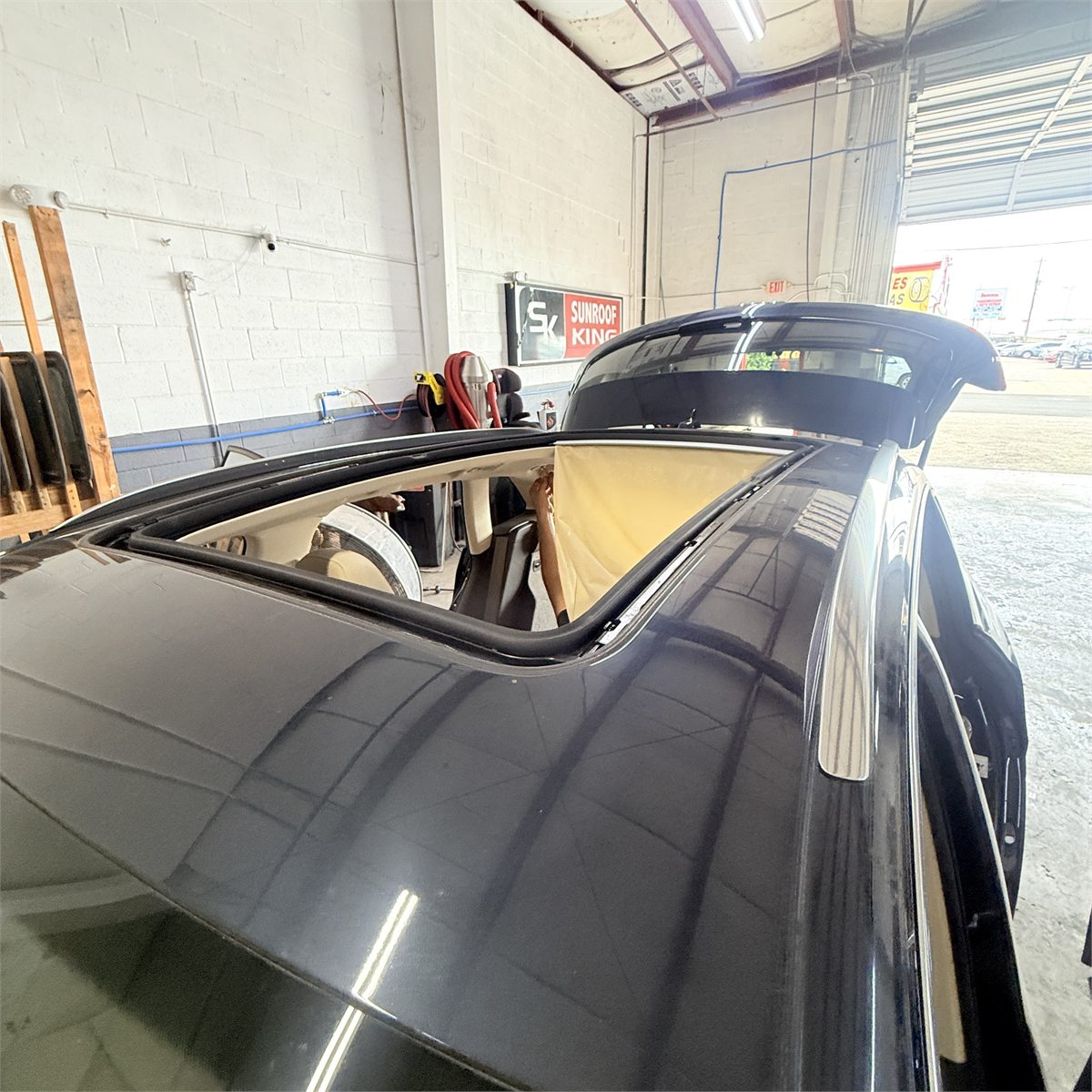 A large sunroof opening on a dark sedan inside the Sunroof King shop in Houston, with the interior covered and protected while the roof assembly is worked on