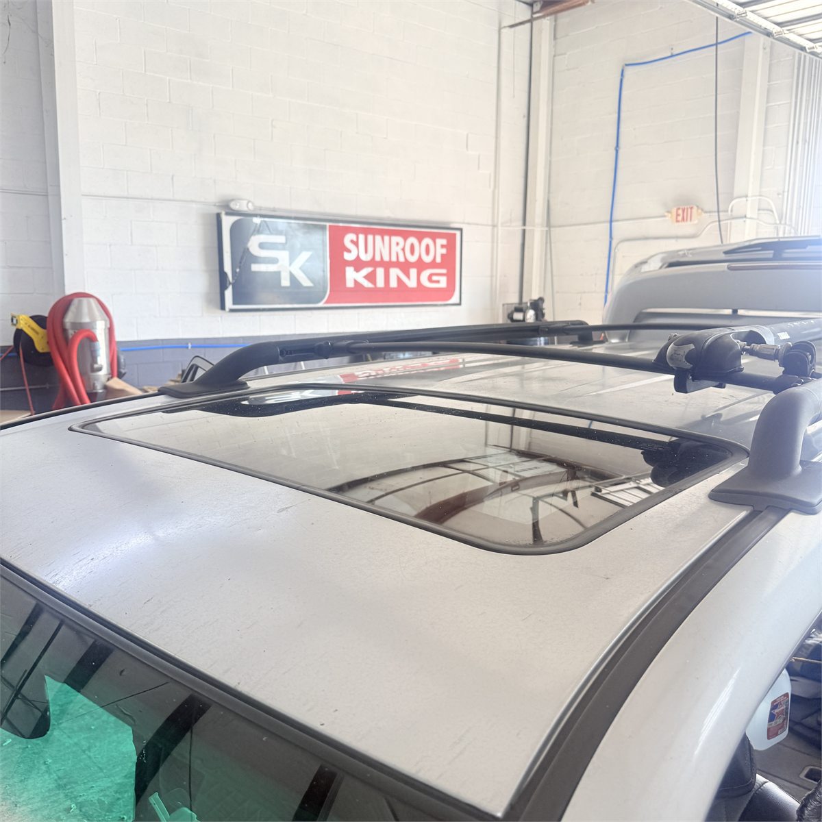 A closed sunroof glass panel in the roof of a silver SUV parked beneath the Sunroof King sign inside the Houston shop