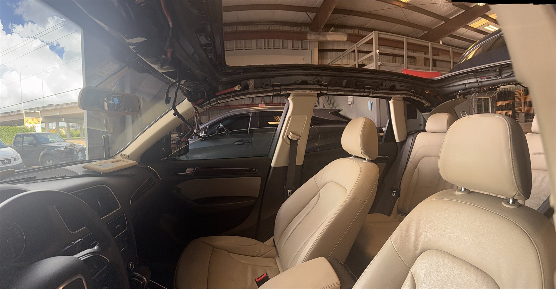 Vehicle interior with the headliner removed at Sunroof King in Houston, exposing the bare roof structure and the panoramic roof cassette above the seats