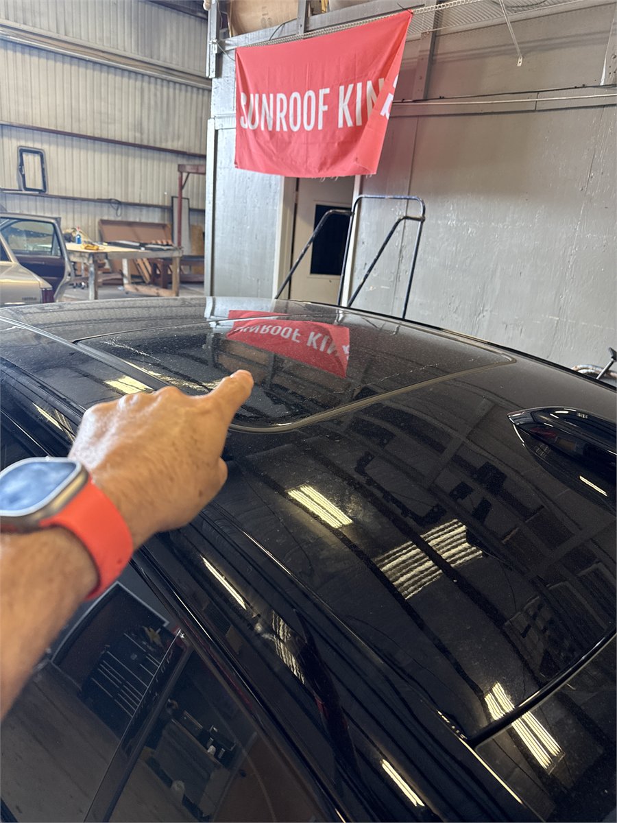 Sunroof King technician pointing out an area of the panoramic roof on a vehicle in the Houston shop while assessing a shade fault