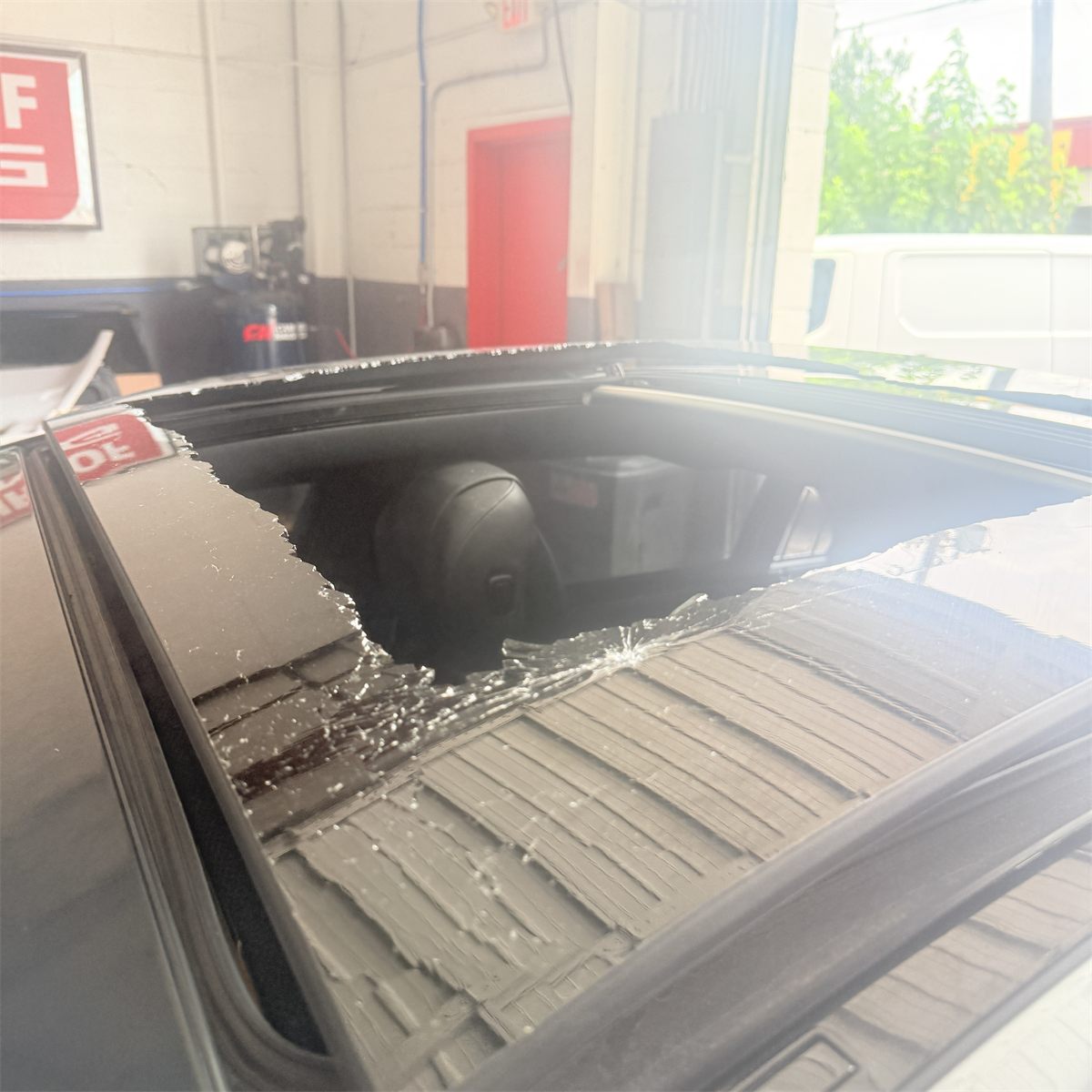 Shattered panoramic sunroof glass on a vehicle at the Sunroof King shop in Houston, broken into small fragments across the panel