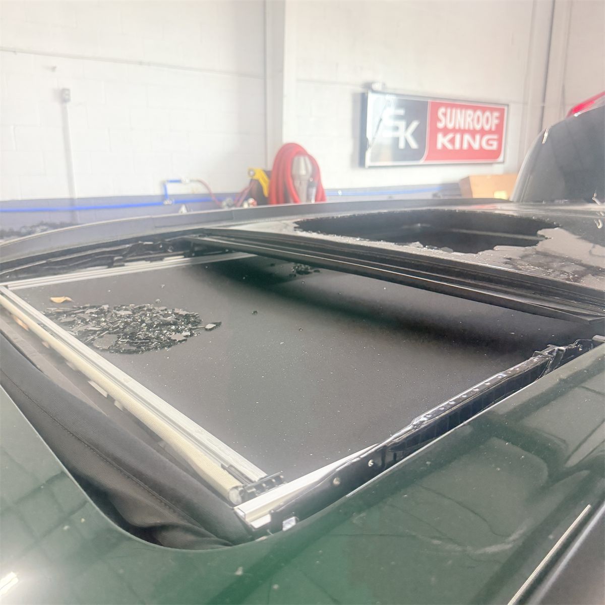 Shattered sunroof glass fragments collected in the roof opening and across the sunshade of a vehicle at Sunroof King in Houston