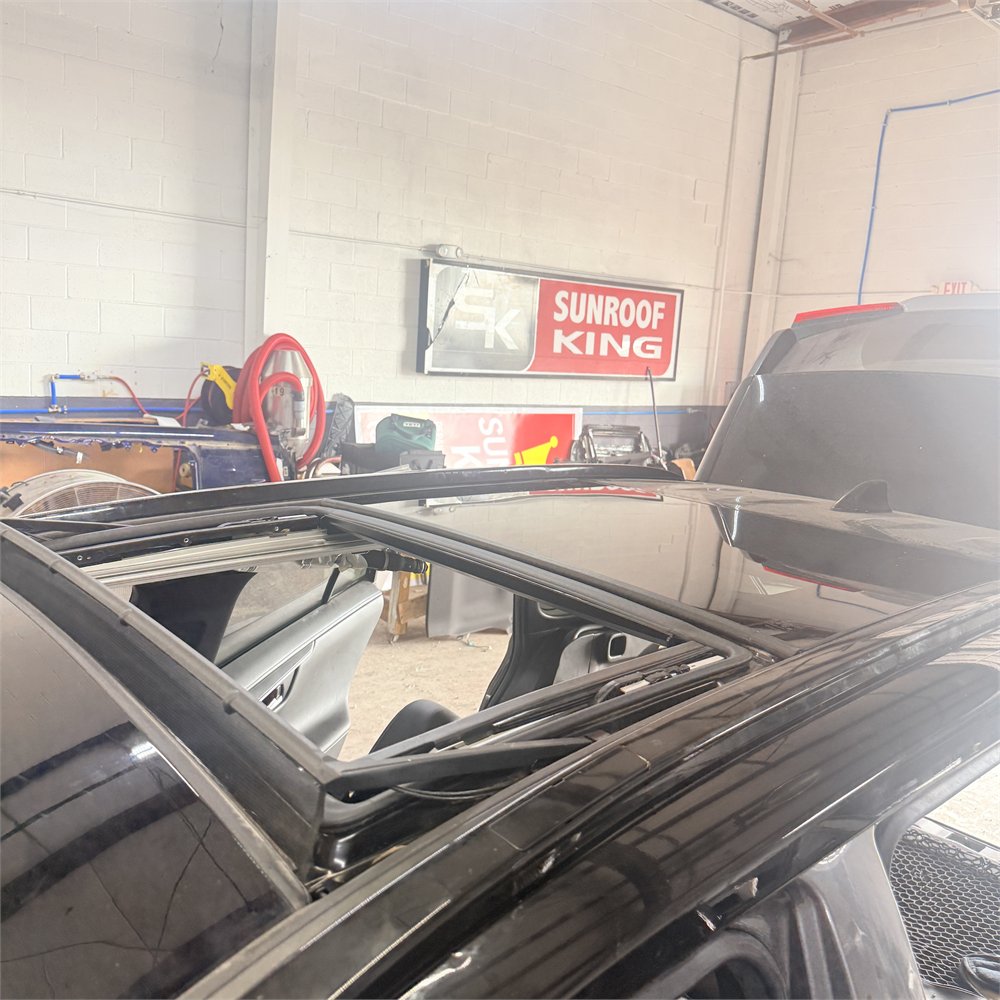 Sunroof glass sitting open and out of line above the roof panel of a car at the Sunroof King shop in Houston