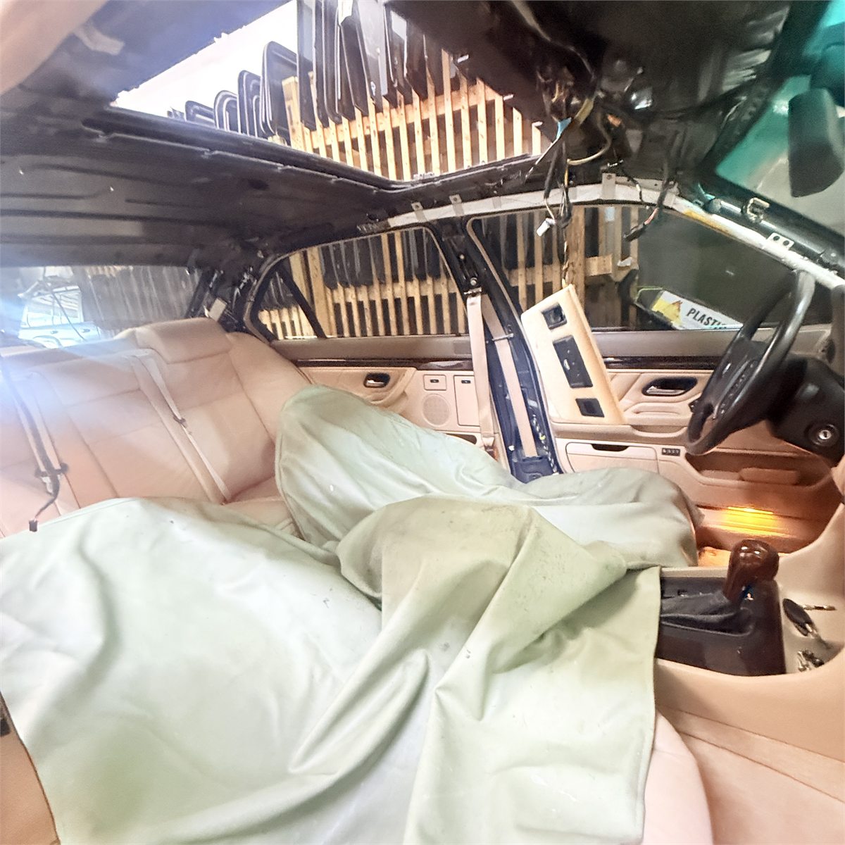 Interior of a sedan at Sunroof King with the headliner removed and the roof frame exposed, and the seats covered with protective sheets before work begins