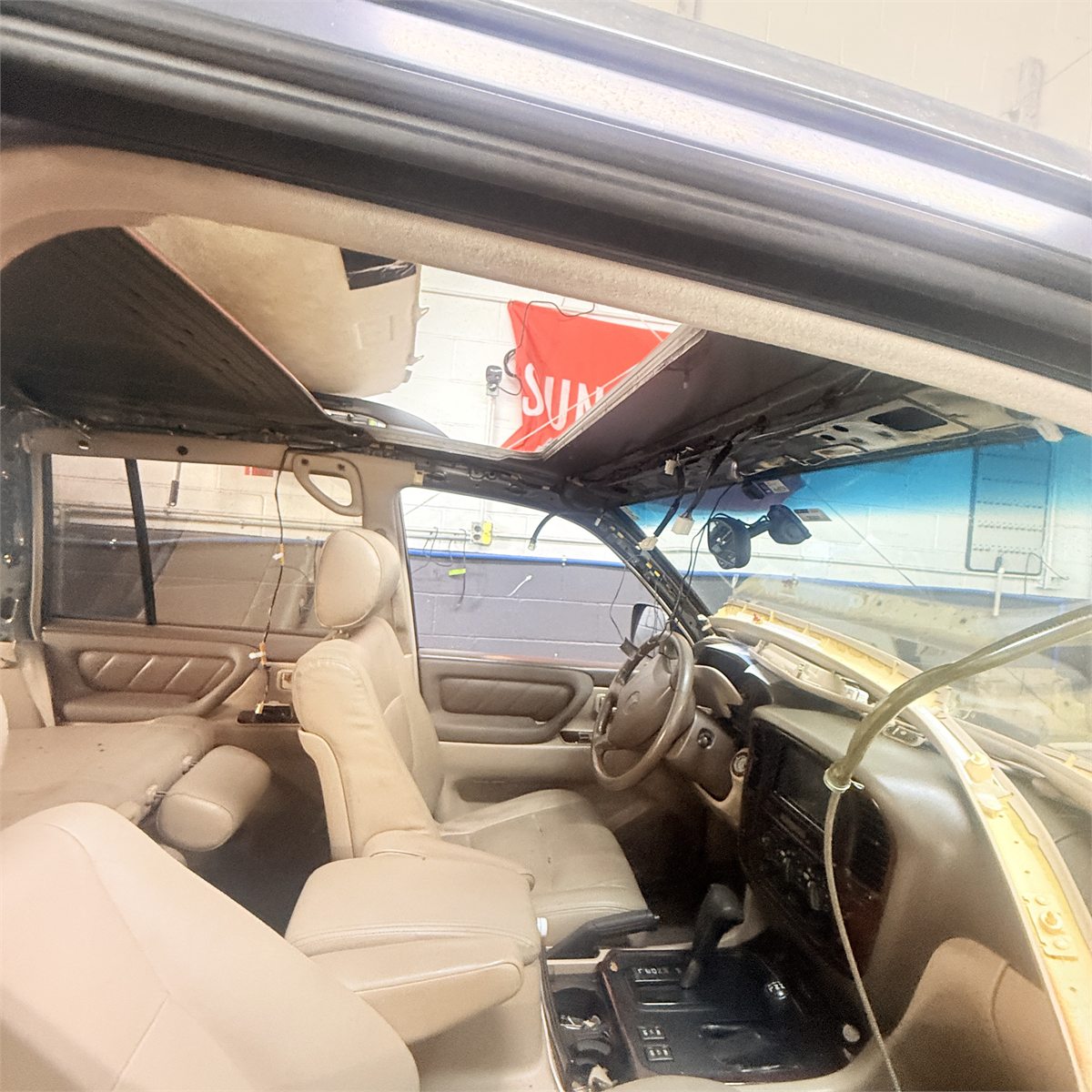 Interior of an SUV at Sunroof King in Houston with roof trim and headliner partly lowered, showing wiring and the open sunroof aperture with the Sunroof King banner visible through it