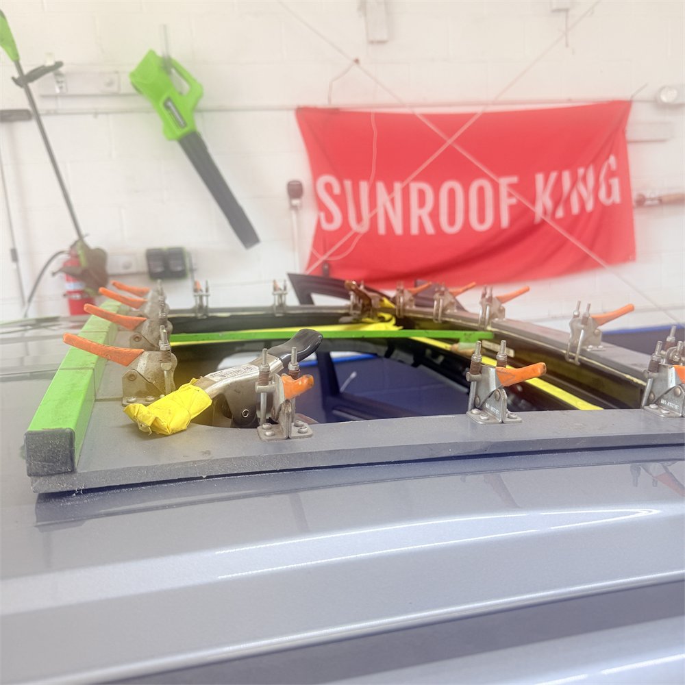 Sunroof aperture on a vehicle roof held under a ring of toggle clamps while the assembly is set at Sunroof King in Houston