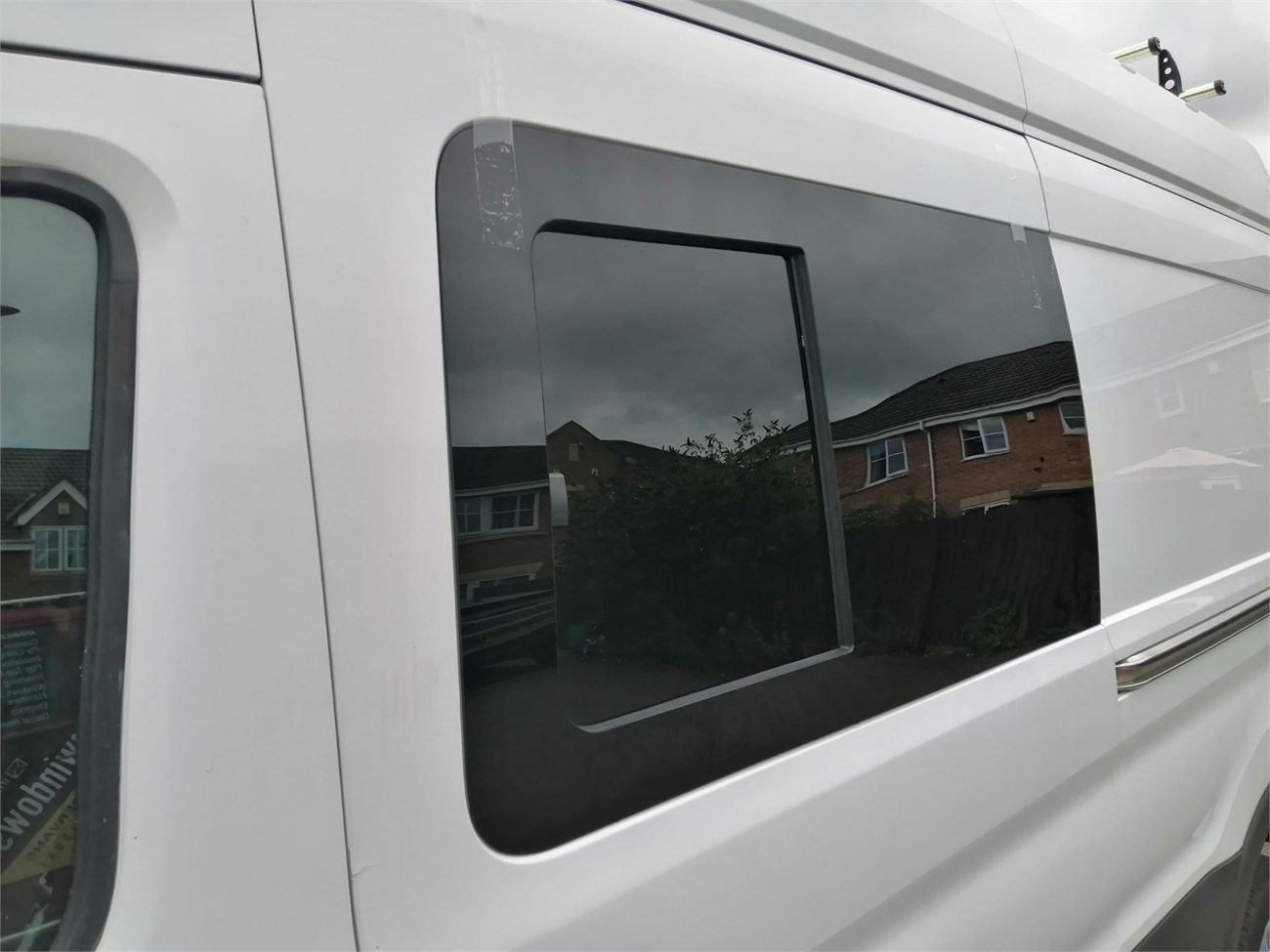 Sliding window fitted into the side panel of a white van, with the opening section visible inside the larger tinted fixed surround