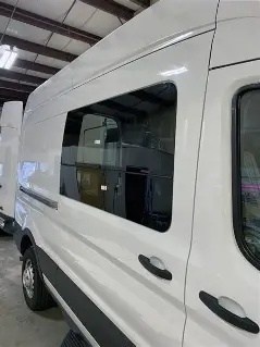Side window fitted into the panel of a white Ford Transit van inside a workshop
